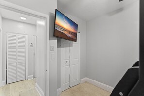 Ein Zimmer mit einem an der Wand befestigten Flachbildfernseher, einer Tür mit weißem Rahmen und einem hellen Boden.
