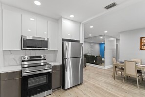 A modern kitchen with stainless steel appliances, a dining area with a table and chairs, and a living room with a sofa and a blue accent wall. - Family Oasis Near Hard Rock Stadium & Beaches (Miami)