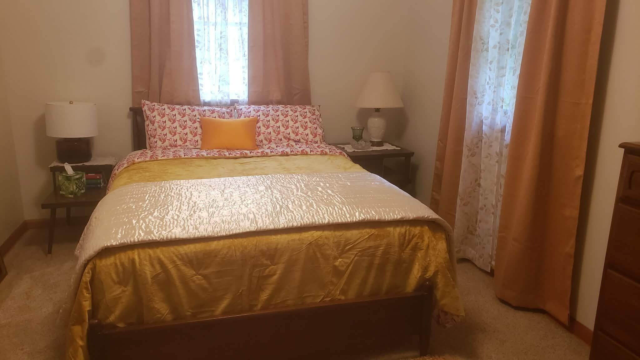 A neatly made bed with a patterned pillow, two bedside lamps, and a nightstand with a tissue box.