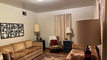 A living room with a sofa, a chair, a lamp, a decorative wall piece, and a window with curtains.