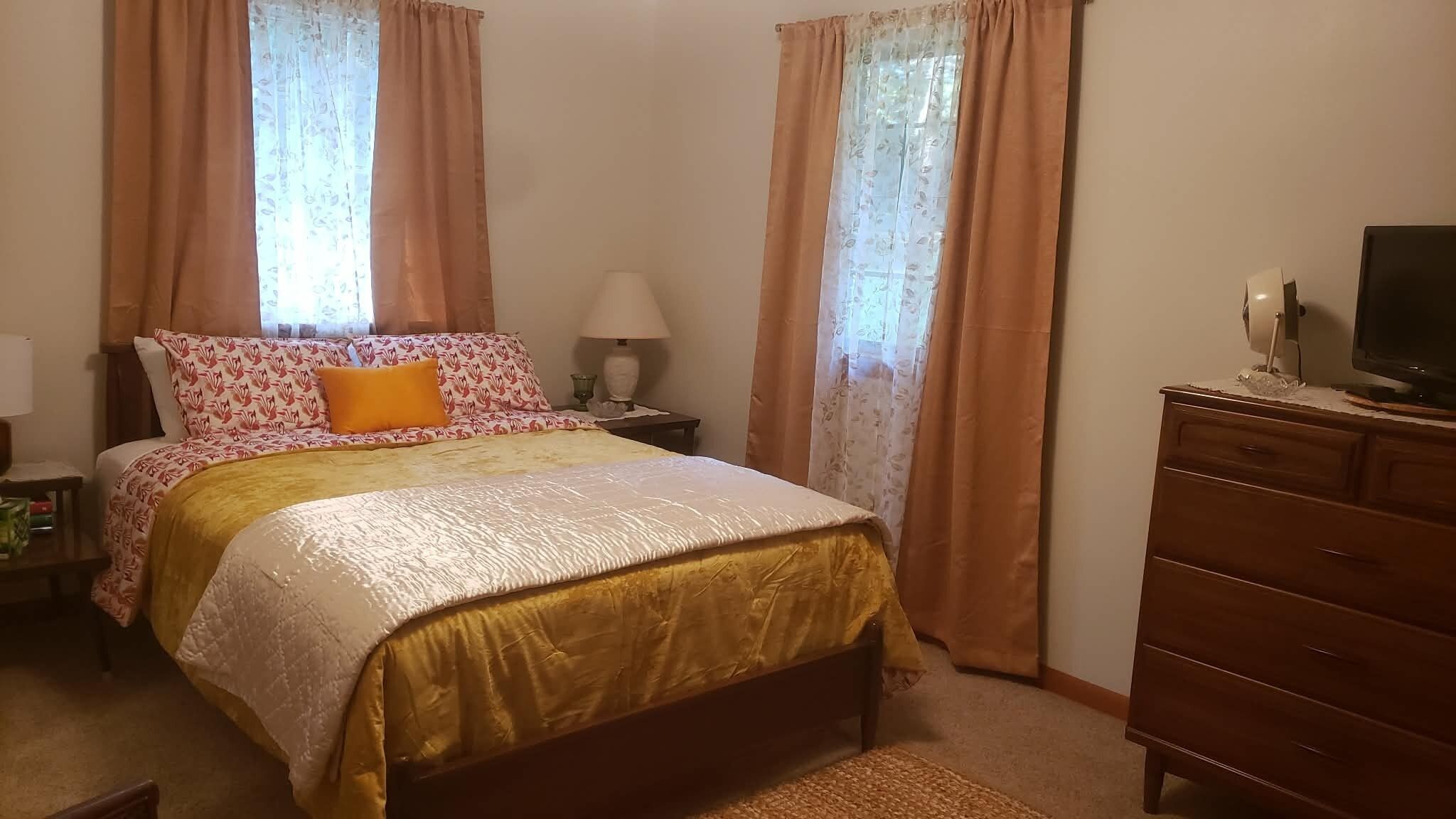 A bedroom with a bed, a nightstand, a lamp, a dresser, and a television.
