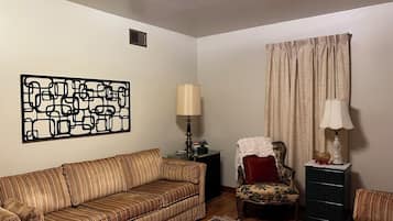 A living room with a striped sofa, a patterned armchair, a small table with a lamp, a decorative rug, and a wall art piece.
