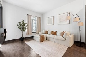 En moderne stue med en hjørnesofa, en potteplante, en gulvlampe og to billeder hængende på væggen.