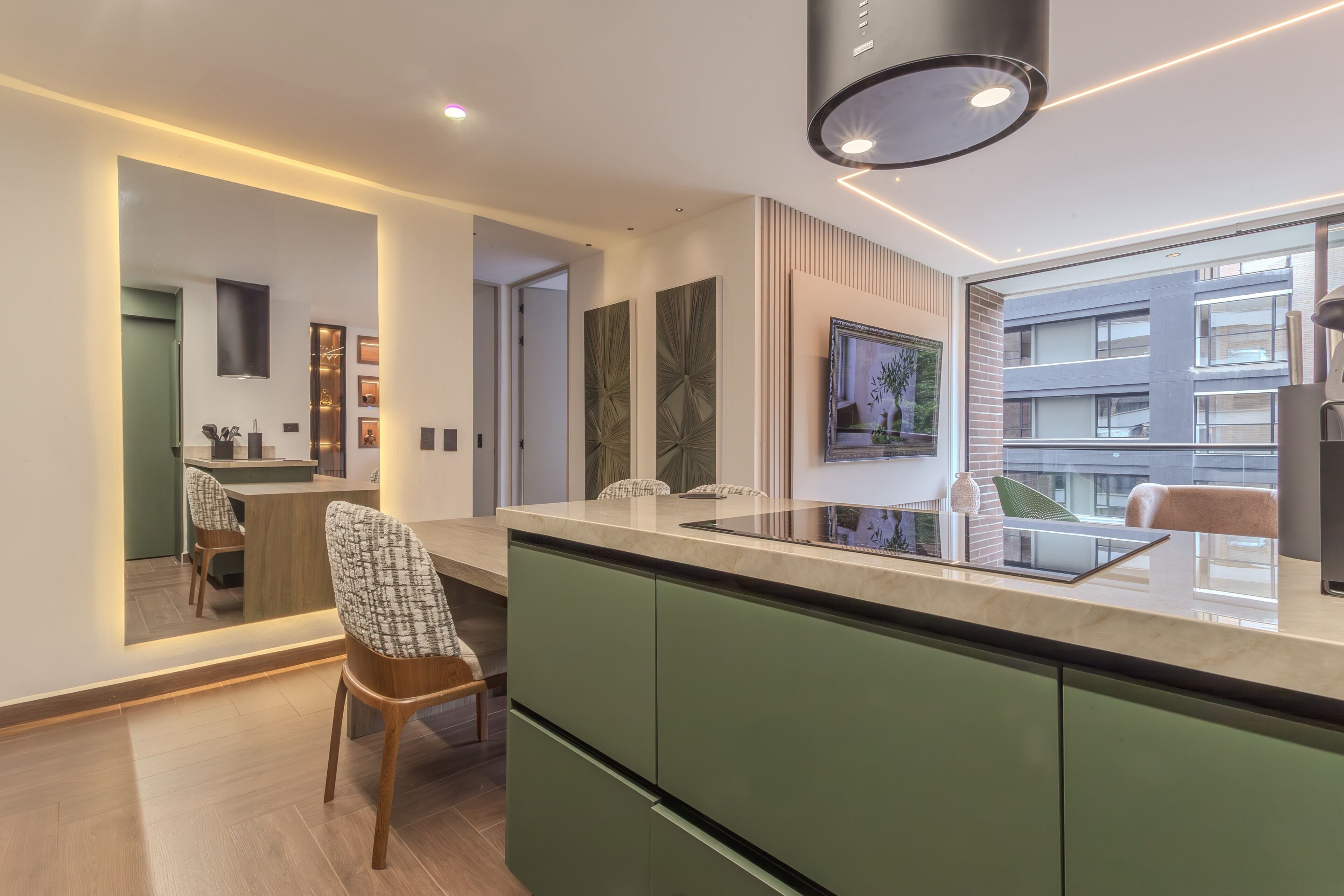 Een moderne keuken met een groot eiland, groene keukenkastjes en een eethoek met een stoel.
