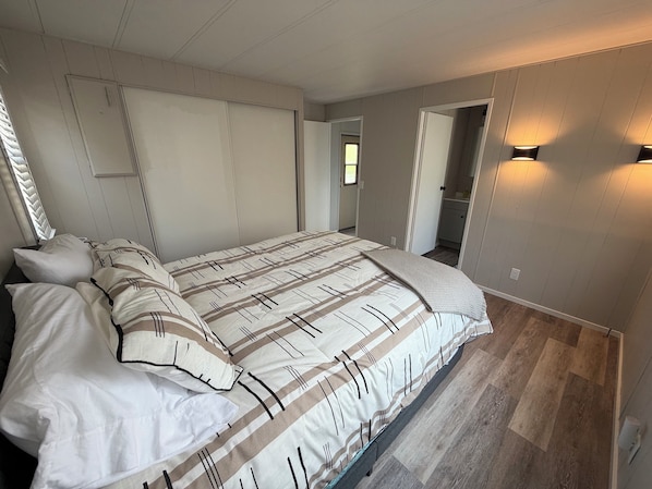 A bedroom with a large bed, a wardrobe, a bathroom, and a hallway.