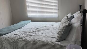 Une chambre à coucher avec un lit, des oreillers, une lampe de chevet et une fenêtre avec des stores.