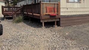 A mobile home with a wooden deck and a red vehicle parked in front.