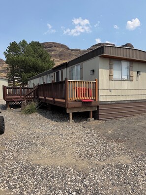 A mobile home with a wooden deck and a red vehicle parked in front.