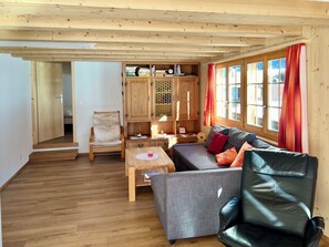 Ein gemütliches Wohnzimmer mit einer Couch, einem Ledersessel, einem Holzschrank und einem kleinen Tisch.