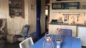 A rustic wooden interior with a dining table, chairs, and a kitchen area with a microwave and utensils. - Kampari - Luxe Safaritent - Titanic by Interhome (Delfstrahuizen)