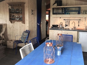 A rustic wooden interior with a dining table, chairs, and a kitchen area with a microwave and utensils. - Kampari - Luxe Safaritent - Titanic by Interhome (Delfstrahuizen)