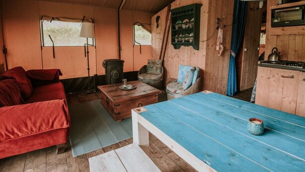 A cozy cabin interior with a sofa, a wooden table, a chair, a lamp, and a kitchenette. - Kampari - Luxe Safaritent - Titanic by Interhome (Delfstrahuizen)