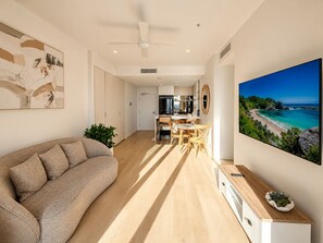 Ein modernes Wohnzimmer mit einer Couch, Essbereich, Küche und einem großen Gemälde von einem Strand.