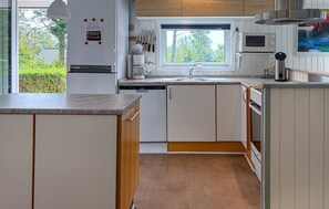 A modern kitchen with white cabinetry, a built-in dishwasher, a microwave, and a window overlooking greenery.