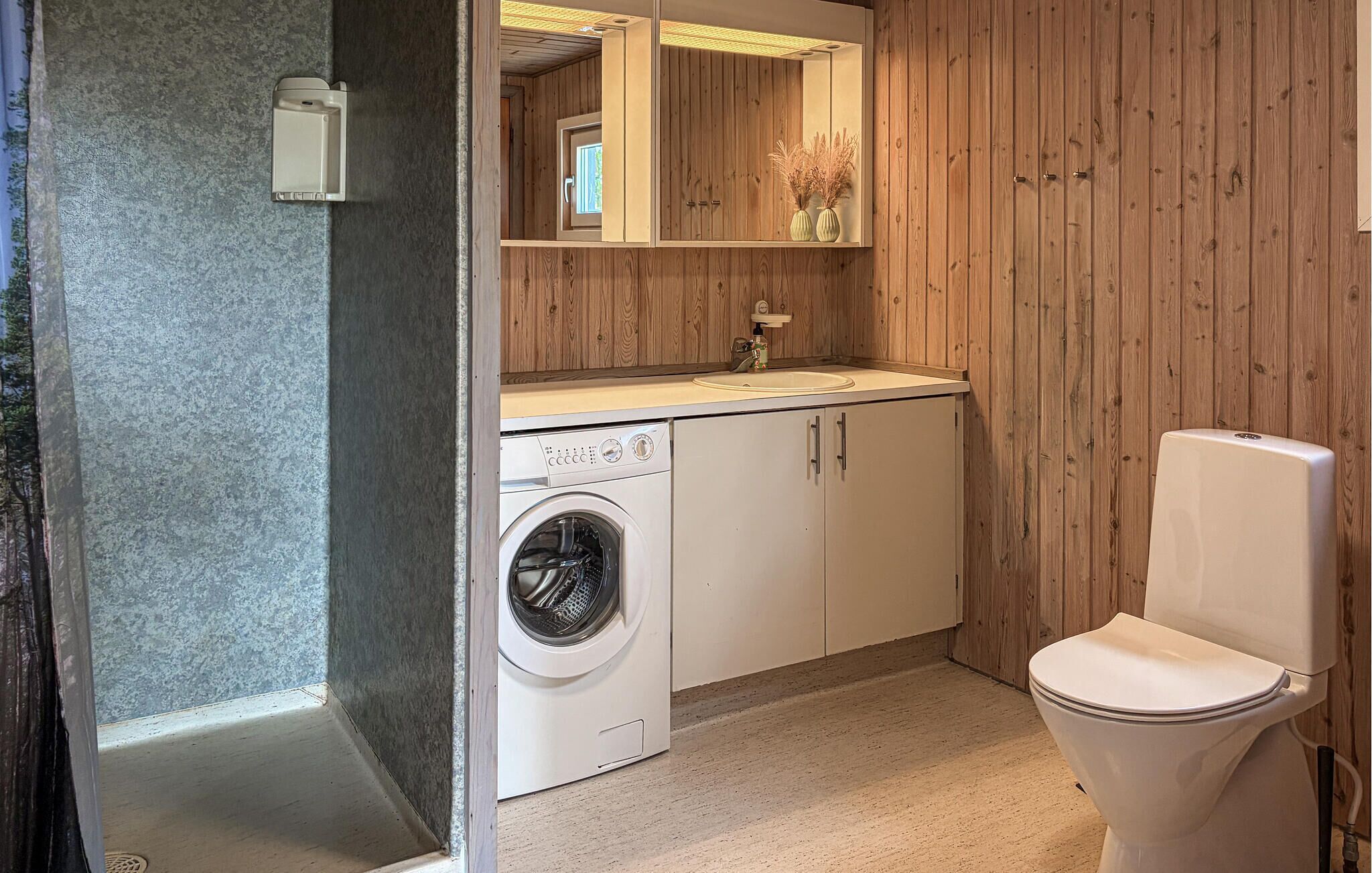 A compact bathroom with a washing machine, a toilet, and a mirror above the sink.