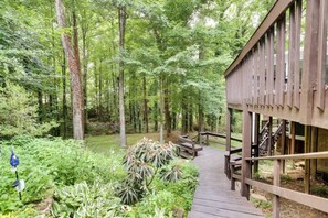 A wooden deck leading to a building with large windows, surrounded by dense forest.