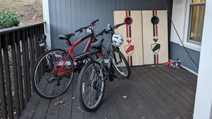Un porche con dos bicicletas, un farol de metal y una tabla de madera con un emblema de gallo.