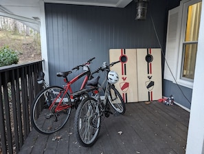 A porch with two bicycles, a metal lantern, and a wooden board with a rooster emblem.