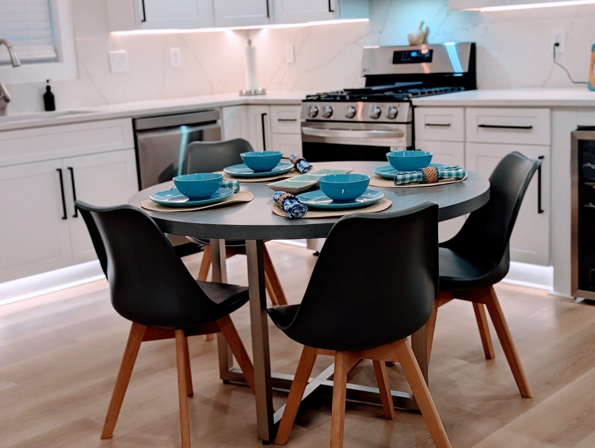 Una cucina moderna con mobili bianchi, piano cottura, forno e un tavolo da pranzo apparecchiato con ciotole e piatti blu.