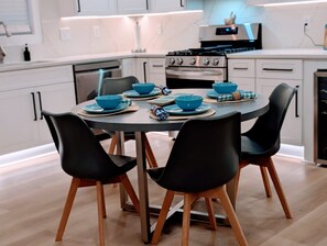 Una cucina moderna con mobili bianchi, piano cottura, forno e un tavolo da pranzo apparecchiato con ciotole e piatti blu.