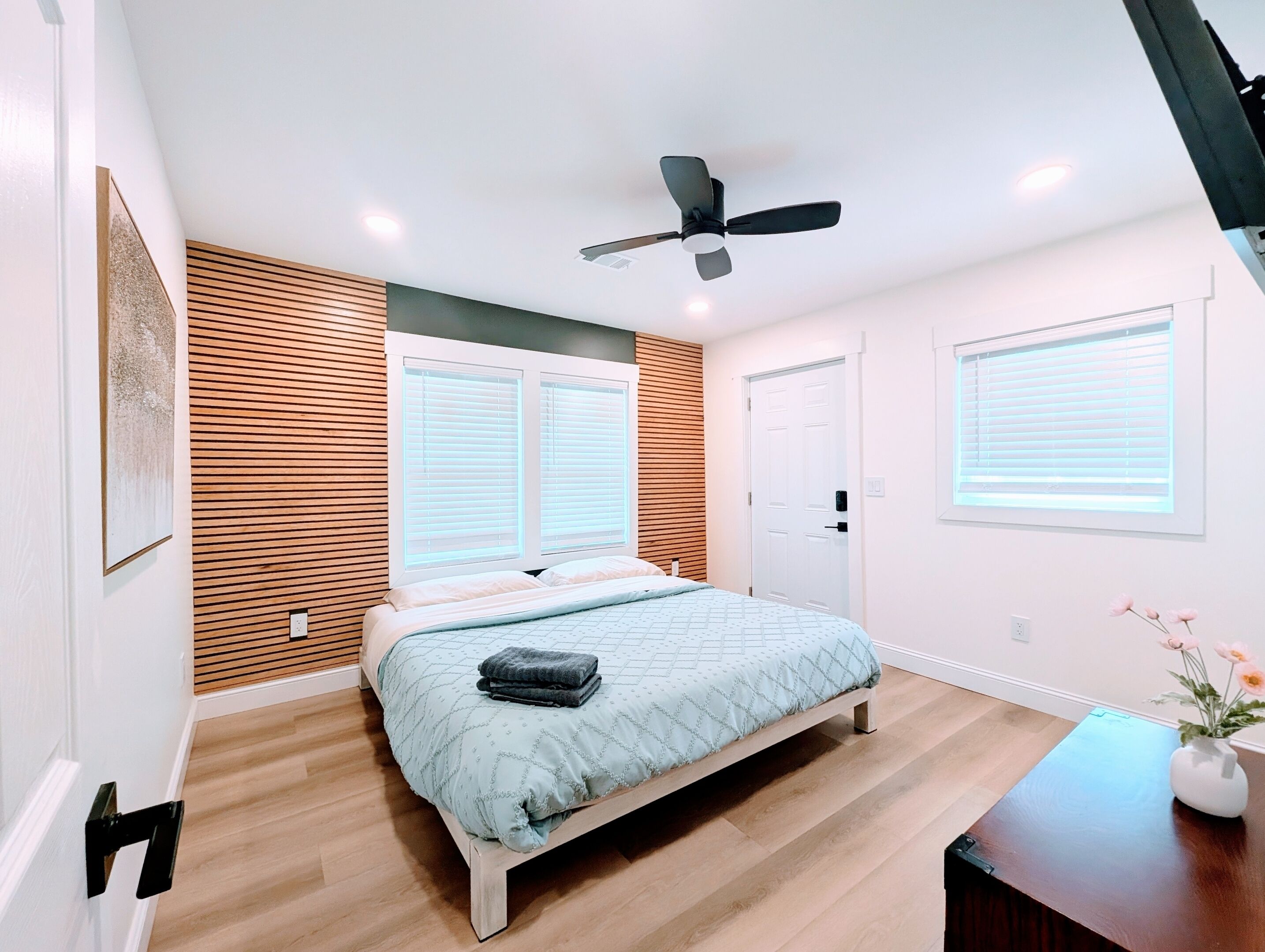 Een slaapkamer met een bed, een plafondventilator en een raam met jaloezieën.