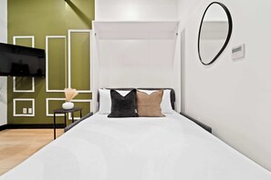 Ein Schlafzimmer mit einem Bett, einem Nachttisch, einem Spiegel und einer Wand mit geometrischen Mustern.