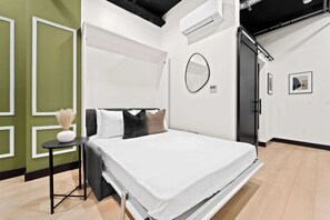 A modern bedroom with a bed, bedside table, and a mirror. - Walk to Petco Park | Gaslamp, Dining & Nightlife!! (San Diego)