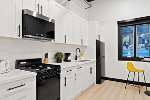 A modern kitchen with white cabinetry, a black stove, a refrigerator, and a window with a city view. - Make Memories Downtown | Walk to Petco Park & Fun! (San Diego)