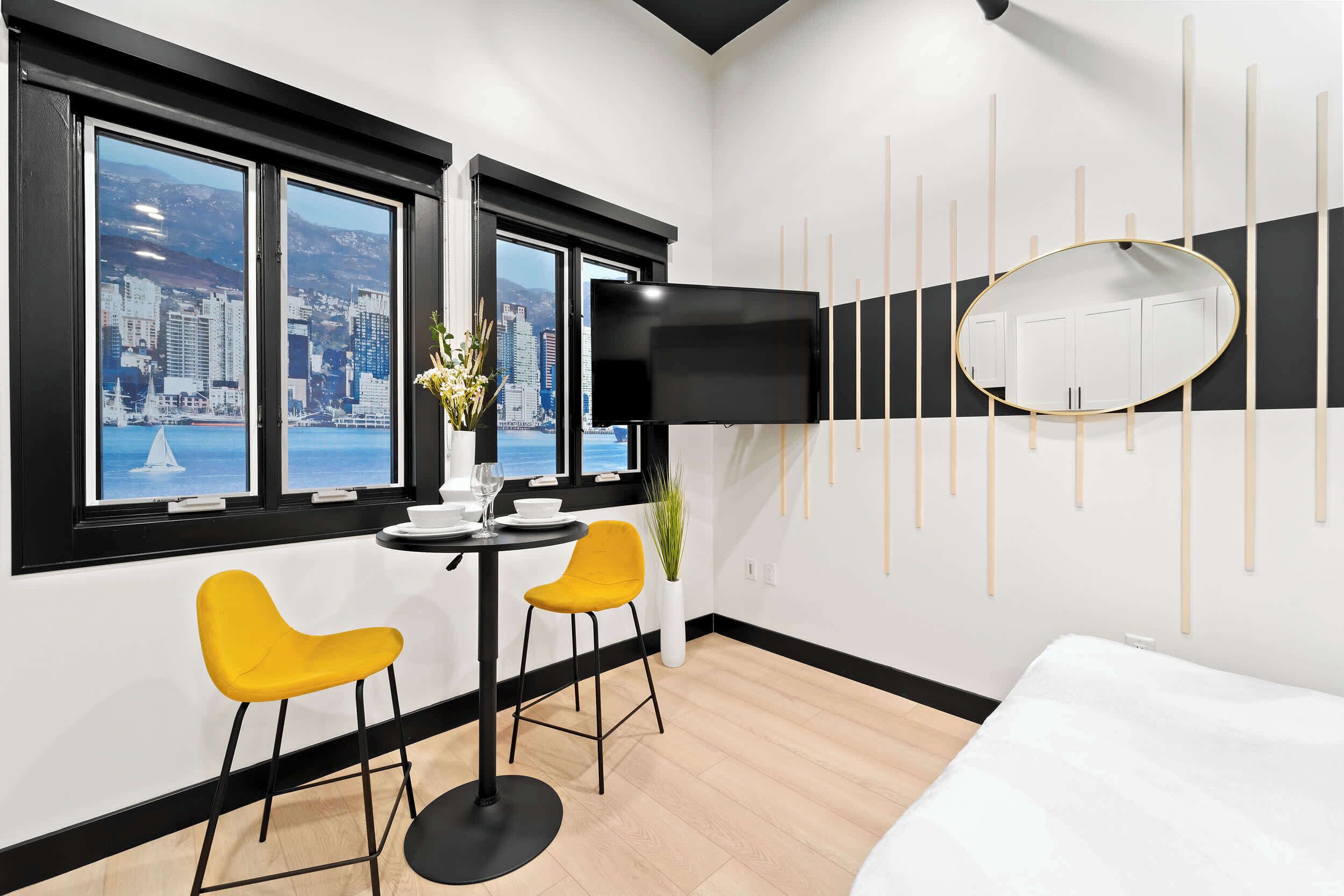 A hotel room with a city view, a TV, a dining area with chairs, and a bed.
