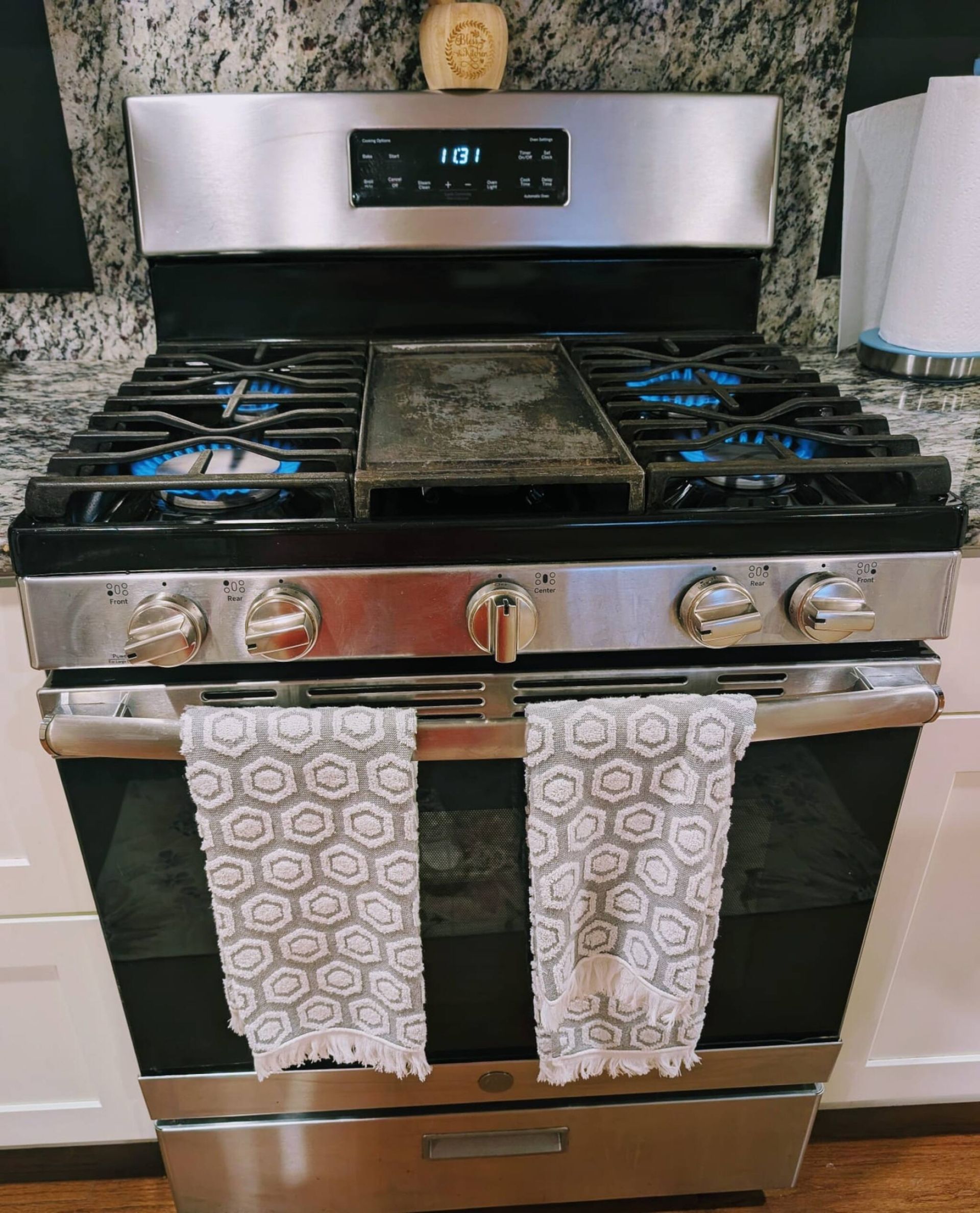 A kitchen with a stainless steel stove, a digital clock, and a granite countertop.
