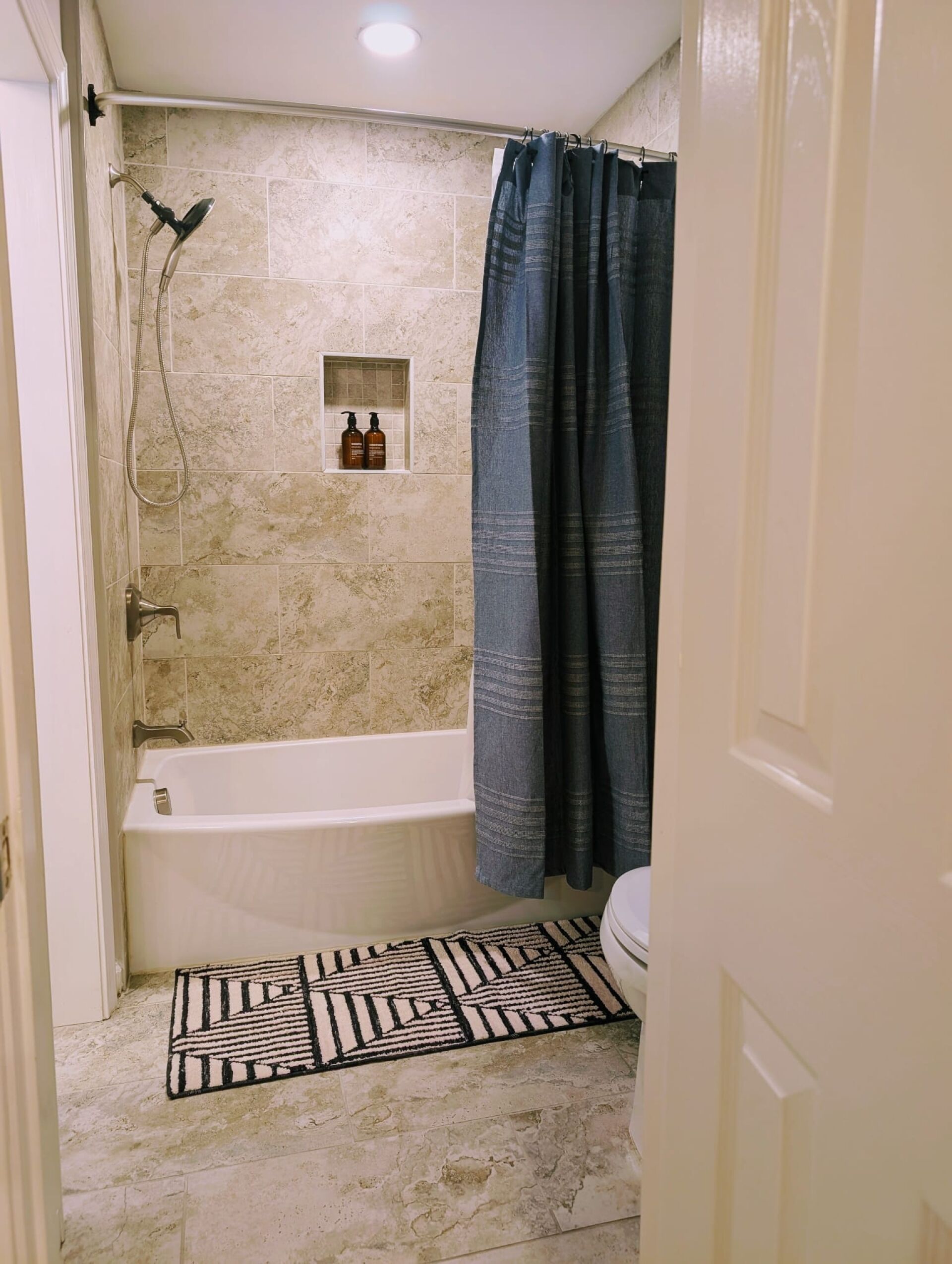 Baño con bañera, ducha y una pequeña ventana con artículos de aseo.