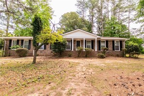 A two-story brick house with a front porch, surrounded by trees and a grassy yard. - Arcade Shuffleboard Poker Firepit Grill @ Battery (Marietta)
