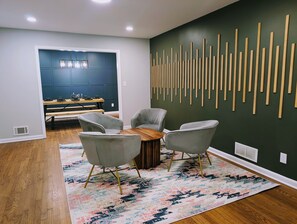 A modern dining area with a wooden table, four grey chairs, and a colorful rug. - Arcade Shuffleboard Poker Firepit Grill @ Battery (Marietta)
