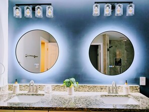 A bathroom with two sinks, a potted plant, and a mirror with a circular frame. - Arcade Shuffleboard Poker Firepit Grill @ Battery (Marietta)