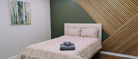 A bedroom with a bed, a ceiling fan, a wall-mounted artwork, and a wooden slat wall design.
