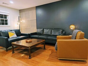 A living room with a dark-colored sofa, a wooden coffee table, and a lamp. - Arcade Shuffleboard Poker Firepit Grill @ Battery (Marietta)