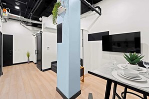 Een modern interieur met een eethoek, een televisietoestel met een zwarte lijst en een plant.