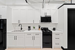 Una cocina moderna con gabinetes blancos, un refrigerador negro, un microondas integrado, una estufa a gas y una cafetera.