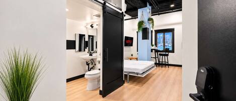 A modern hotel room with a bed, a desk, a chair, a TV, and a bathroom with a toilet and sink.