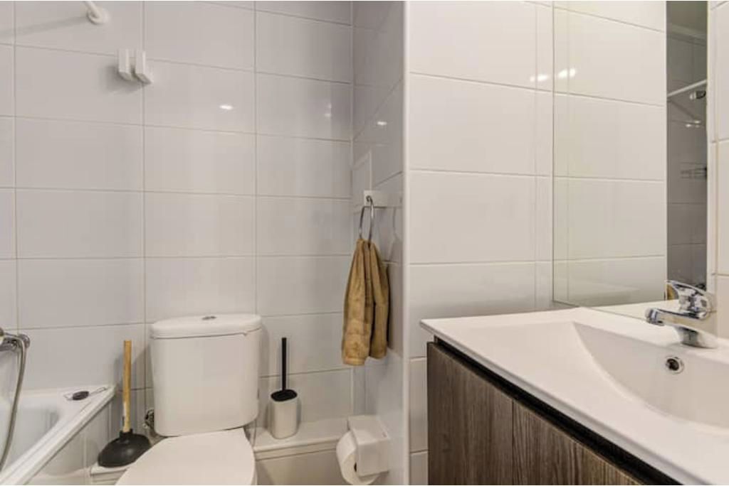 Ein Badezimmer mit weißen Fliesen, einer Toilette, einem Waschbecken und einem Spiegel.
