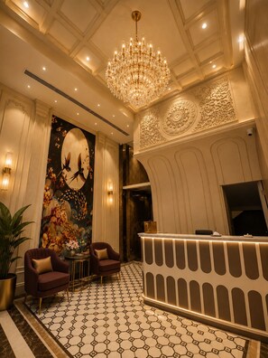 A lobby with a chandelier, a reception desk, and a mural. - Purple Martin by AVSA Stayz (Amritsar)