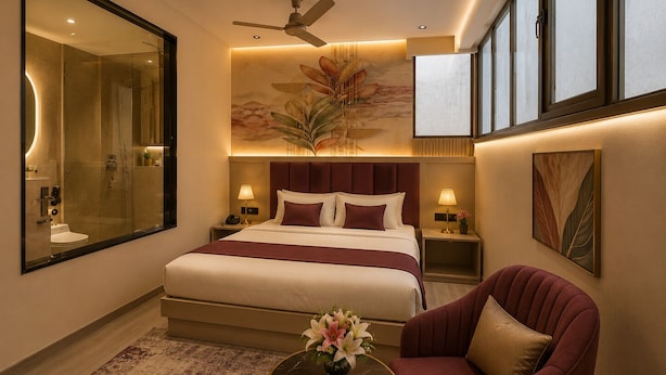 Habitación de hotel con una cama grande, una zona de estar con una silla, una mesa de centro redonda, un espejo grande y un ventilador de techo.
