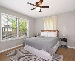 A bedroom with a bed, a ceiling fan, two bedside tables, and a window with blinds. - Charming 2-bedroom house in beautiful College Station 2 miles from campus. (College Station)