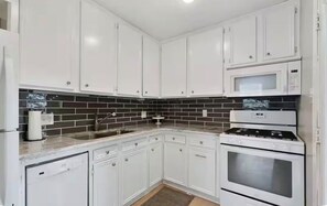 A kitchen with white cabinets, a black and white backsplash, a microwave, and a stove. - Charming 2-bedroom house in beautiful College Station 2 miles from campus. (College Station)