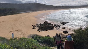 Une plage bordée d’une côte rocheuse, une plage de sable et, en arrière-plan, une colline boisée.