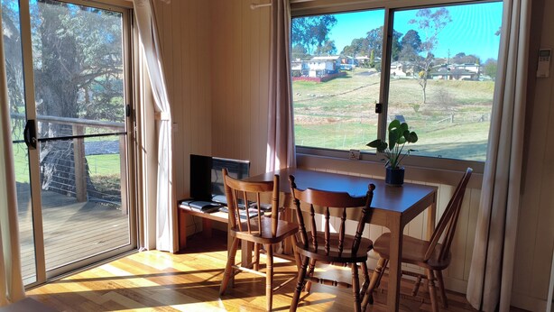A room with a wooden floor, a dining table with chairs, a television, and a window with curtains.