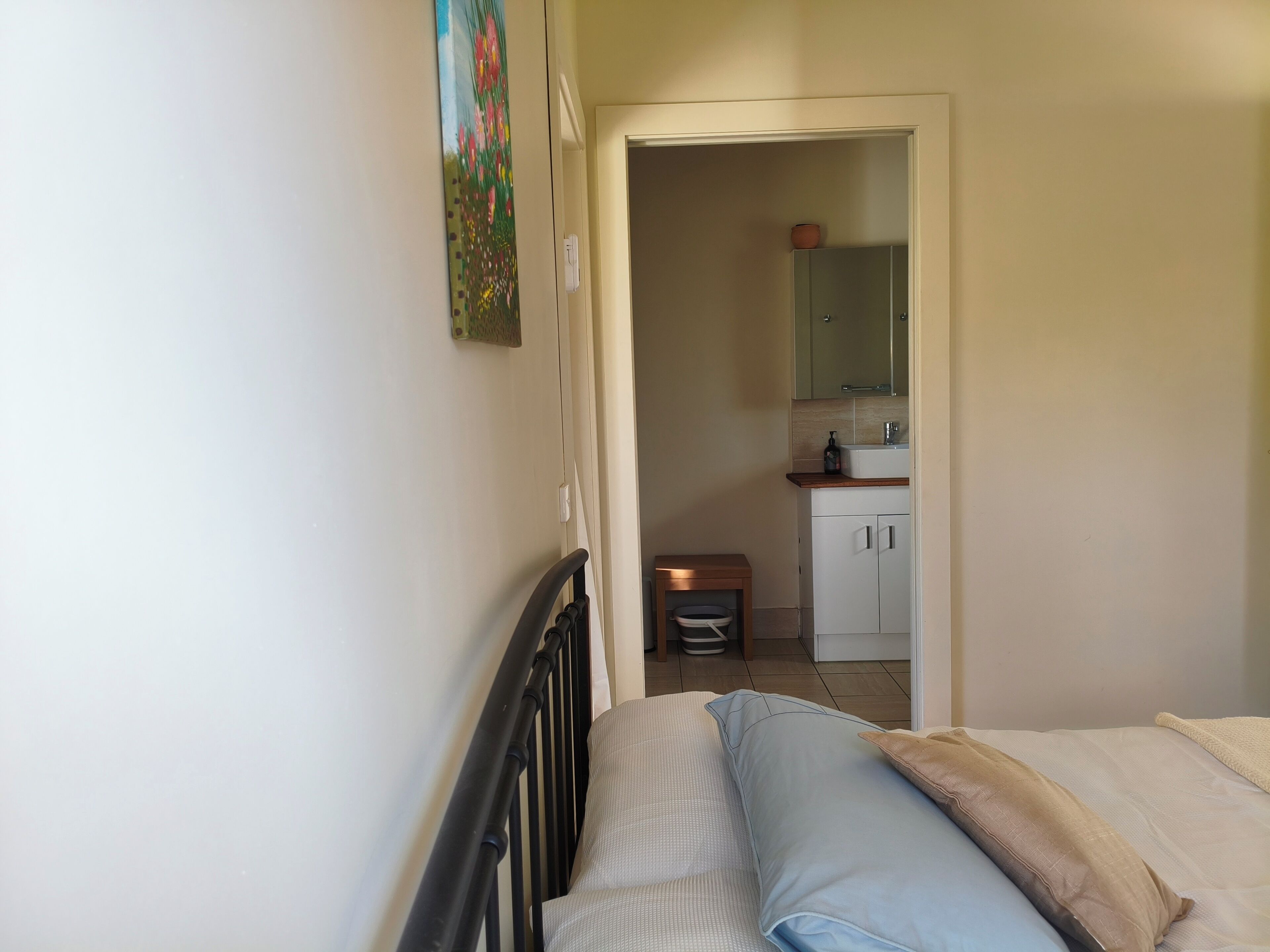 A bedroom with a bed, a nightstand, a small table with a chair, a mirror, and a door leading to a bathroom.