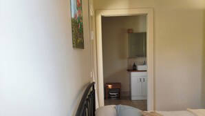 A bedroom with a bed, a nightstand, a small table with a chair, a mirror, and a door leading to a bathroom.