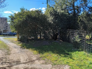 Un sendero de tierra que conduce a un área cercada con árboles frondosos y un cielo despejado.