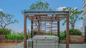 A modern outdoor seating area with a metal pergola structure, a cushioned bench, and a small table. - Ardana by Kozystay - Tunjungan (Surabaya)